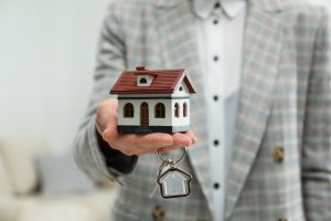 Real,Estate,Agent,Holding,House,Model,And,Key,Indoors,,Closeup